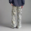 A person wearing Cargo Pants Y2K Fashion Side Pockets from Kanye Streetwear Store, featuring a camouflage design and numerous pockets, stands with their back to the camera. The plain gray background adds an air of mystery to the scene.