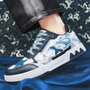 A close-up of the Vexlly Men Casual Sneakers Trend Skateboard Flat Outdoor Shoes showcases a blue and white design adorned with star and dragon motifs, ideal for casual wear. The sneakers feature blue laces and a white sole with dark blue trim, worn by someone in black jeans against a patterned backdrop.