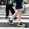 Two people are walking side by side on a crosswalk. Both are donning casual outfits with Vexlly's Colorblock Patterned Sneakers in Blue. One is carrying a small blue Nike bag. The scene appears urban, and the focus is on their legs and footwear.