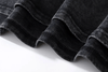 Close-up of the folded edges of black, faded denim fabric displayed on a white background, highlighting the texture and stitching details similar to those found on the Vexlly Voltgmann Chaotic Space Vintage Graphic Tee.