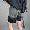 A person wearing the Vexlly Summer Gradient Denim Shorts in black ombre and a black shirt, carrying a black backpack over one shoulder, stands against a gray background. Be sure to check the size chart for reference, as sizes are based on Asian measurements.