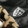 Close-up of a Vexlly Fuzzy Cheetah Camouflage Patchwork Fleece Jacket in black leather with a white "BUFF" crest and fleur-de-lis emblem, accompanied by an area of soft camouflage-patterned faux fur fabric.