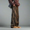 A person dressed in Vexlly's Leopard Print Jeans Men Fashion Retro Wide Leg, paired with tan boots, a brown sweatshirt, and a gray sling bag stands against a neutral background. Be sure to consult the clothing size chart for Asian sizes to ensure the perfect fit. Their face and upper body remain out of view.