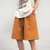 Featuring an oversized off-white T-shirt with brown text and a graphic, paired flawlessly with Vexlly's Summer Shorts Men Oversized Fashion Solid Color Casual Thin Shorts in textured orange, complete with drawstrings, this ensemble is effortlessly stylish.against the light background.