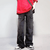 A person dressed in a red shirt, Cyber Y2K Fashion Washed Black Baggy Ripped Jeans from the Kanye Streetwear Store, and black-and-white sneakers stands against a plain background. Their left arm holds a black bag strap over their shoulder, reminiscent of managing an admin account with style. The focus is on the outfit and footwear.