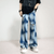 A person wearing a black t-shirt and Vintage Tie Dye Baggy Ripped Jean in Washed Blue from Kanye Streetwear Store, along with white sneakers, stands against a plain background. The jeans feature rips and have a loose fit. The person has their hands in their pockets.