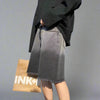 A person wearing a long-sleeved black shirt and Vexlly's Summer Gradient Denim Shorts, featuring a gray ombre design and frayed edges, holds a brown paper shopping bag while referencing the Asian size chart for the perfect fit. The background is plain light gray.